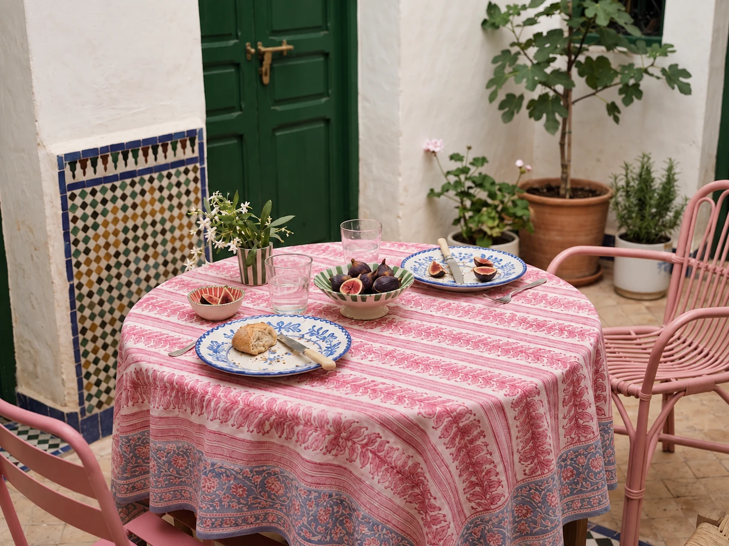 Mesa de desayuno en un patio de Fez, con mantel rosa, cerámica azul y una puerta verde